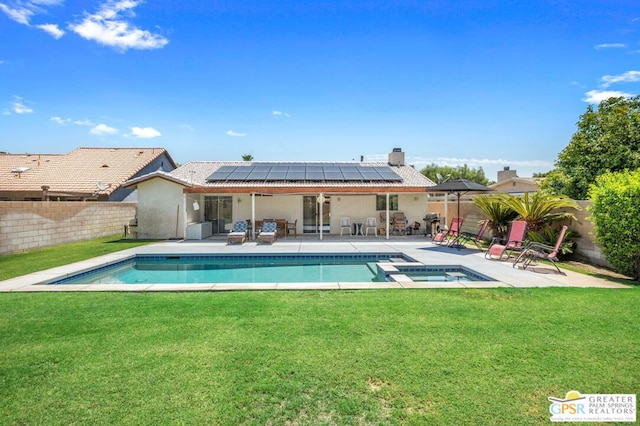 rear view of property with a lawn, a swimming pool with hot tub, solar panels, and a patio