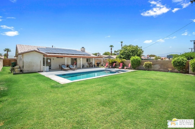 rear view of property with a lawn, a patio, solar panels, and a fenced in pool