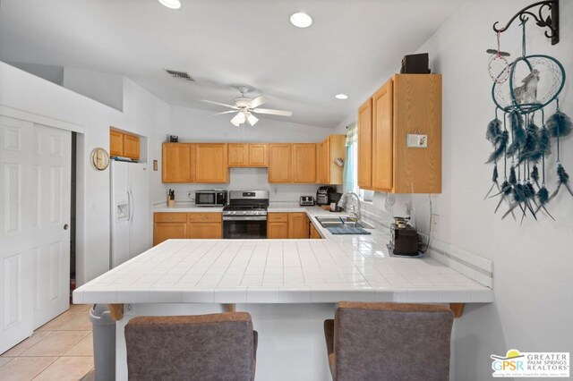 kitchen with kitchen peninsula, ceiling fan, appliances with stainless steel finishes, vaulted ceiling, and sink