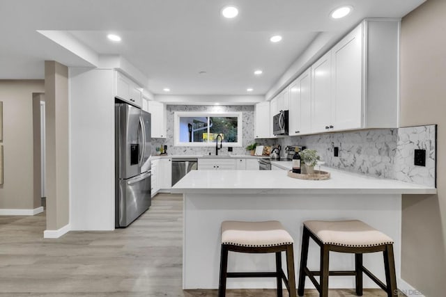 kitchen featuring kitchen peninsula, appliances with stainless steel finishes, a kitchen breakfast bar, and white cabinetry