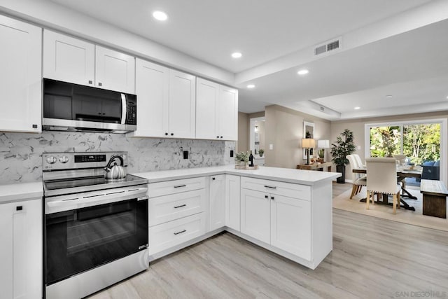 kitchen featuring appliances with stainless steel finishes, white cabinetry, kitchen peninsula, a raised ceiling, and light hardwood / wood-style flooring