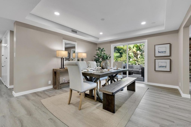 dining room with a tray ceiling and light wood-type flooring