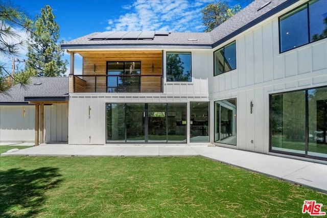 rear view of house with a lawn, solar panels, a patio area, and a balcony