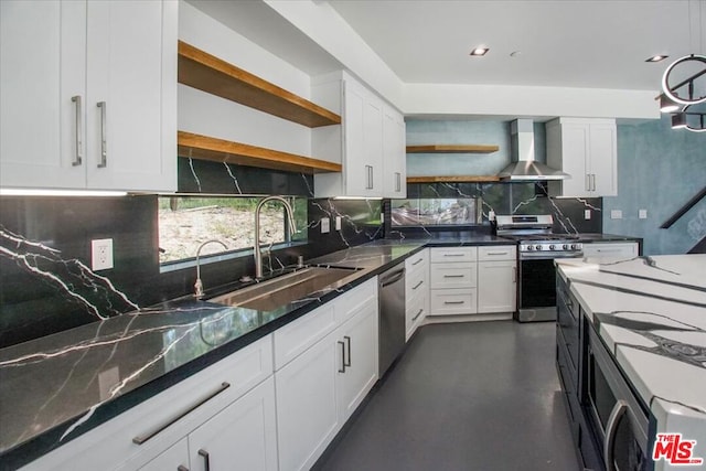 kitchen with white cabinetry, wall chimney range hood, stainless steel appliances, dark stone counters, and sink