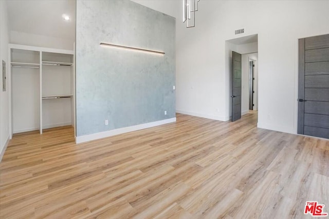 unfurnished bedroom with a high ceiling, light hardwood / wood-style flooring, and a closet