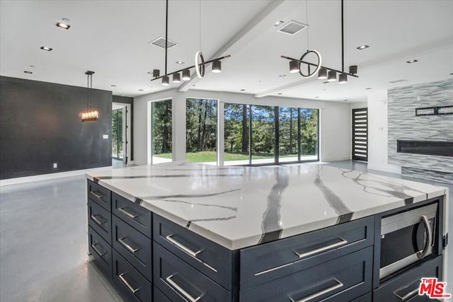 kitchen featuring stainless steel microwave, concrete floors, a premium fireplace, hanging light fixtures, and light stone countertops