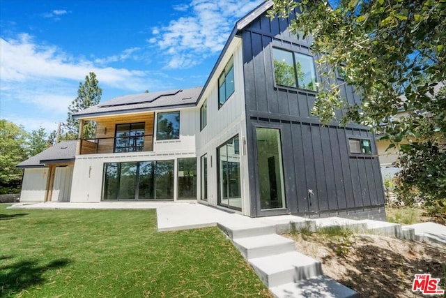 back of house featuring solar panels, a balcony, and a yard