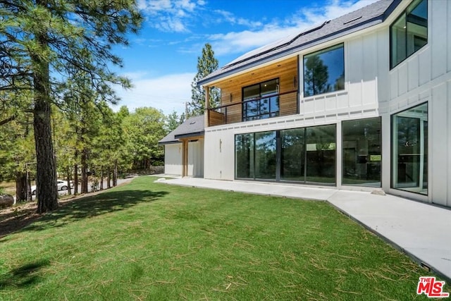 rear view of house with a balcony, a lawn, and a patio