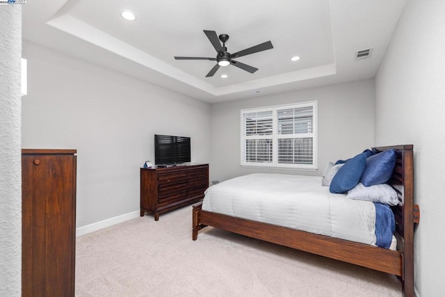 bedroom with ceiling fan, light carpet, and a tray ceiling