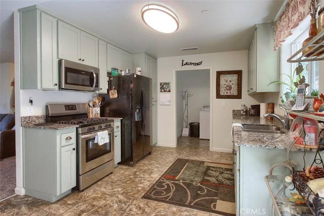 kitchen with washer / clothes dryer, white cabinetry, stainless steel appliances, dark stone counters, and sink