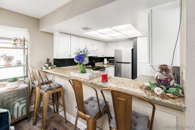 kitchen with light stone countertops, kitchen peninsula, white cabinets, and stainless steel appliances