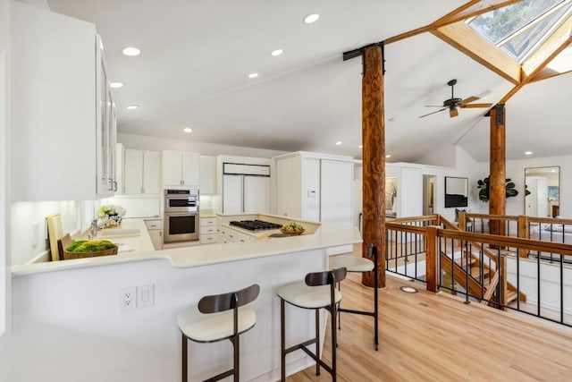 kitchen featuring white cabinetry, kitchen peninsula, stainless steel appliances, vaulted ceiling with skylight, and sink