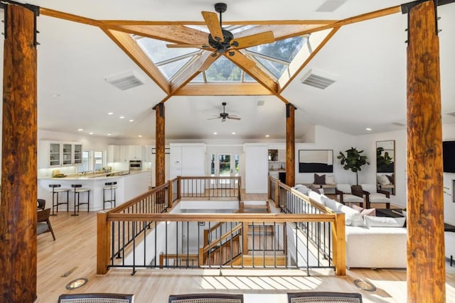 living room with ceiling fan, vaulted ceiling with skylight, and light hardwood / wood-style floors