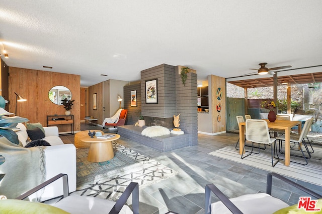 living room featuring ceiling fan, wooden walls, and a textured ceiling