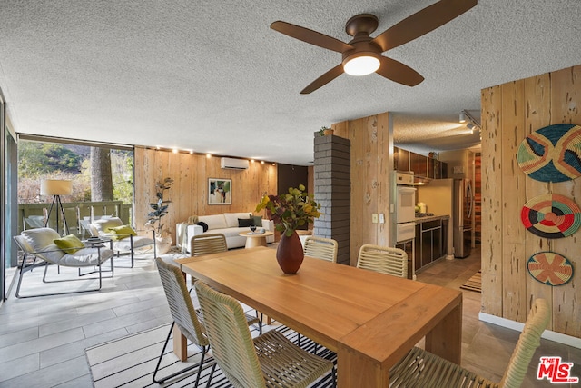 dining room featuring a textured ceiling, ceiling fan, a wall mounted AC, and wood walls