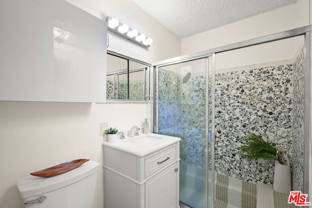 bathroom with a textured ceiling, toilet, a shower with door, and vanity