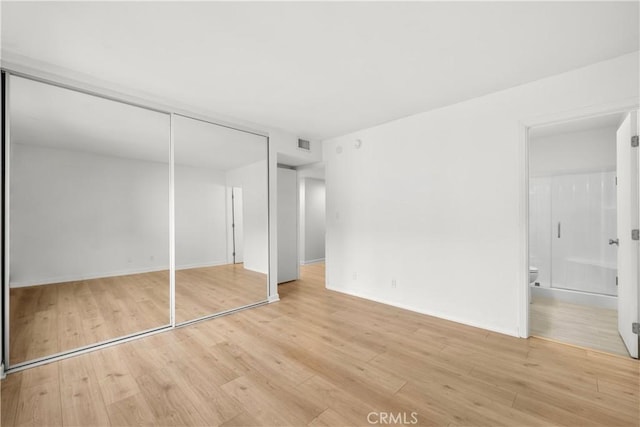 unfurnished bedroom featuring ensuite bath, a closet, and light hardwood / wood-style flooring