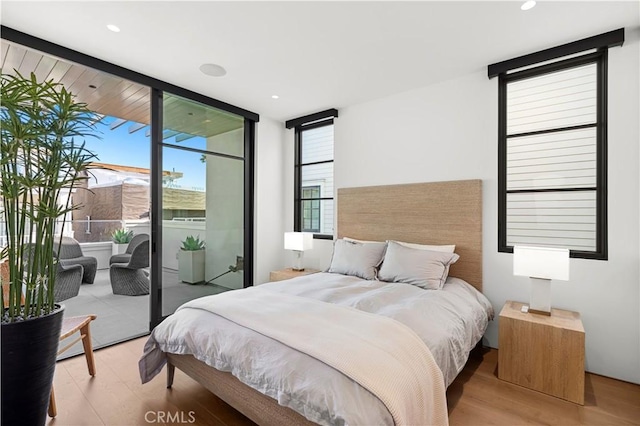 bedroom featuring light wood-type flooring, access to exterior, and a wall of windows