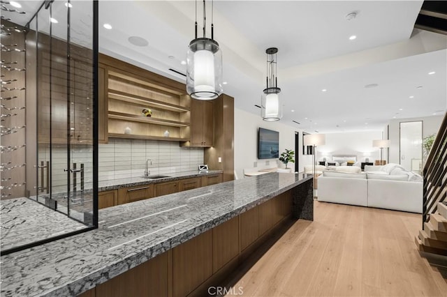 kitchen featuring decorative backsplash, decorative light fixtures, light wood-type flooring, dark stone countertops, and sink