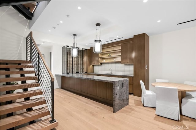 kitchen featuring tasteful backsplash, pendant lighting, sink, light wood-type flooring, and light stone counters