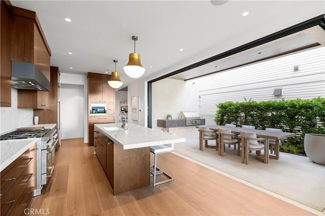 kitchen featuring an island with sink, pendant lighting, stainless steel stove, light hardwood / wood-style flooring, and sink