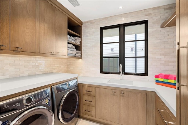 clothes washing area featuring cabinets, washing machine and clothes dryer, and sink