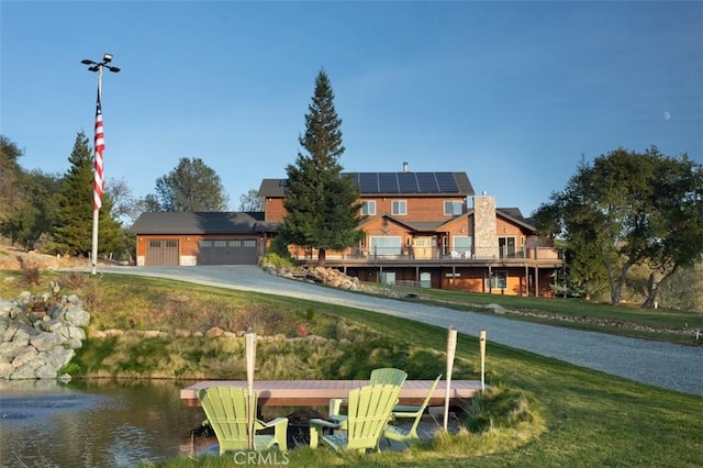 back of property with a water view, roof mounted solar panels, and a lawn