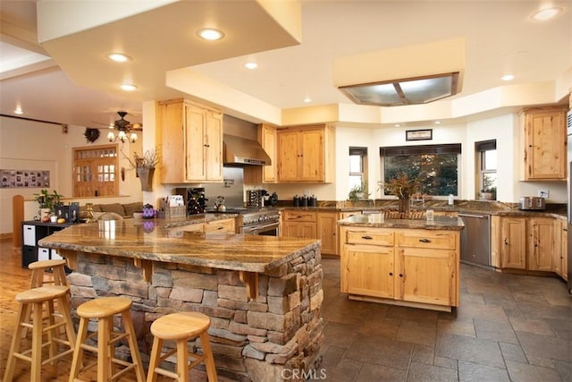 kitchen featuring a breakfast bar area, light brown cabinets, a peninsula, stainless steel appliances, and wall chimney exhaust hood