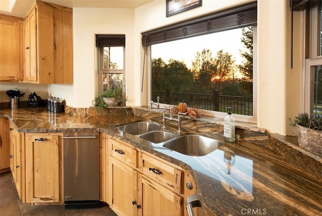 kitchen featuring light brown cabinets, dark stone countertops, and a sink