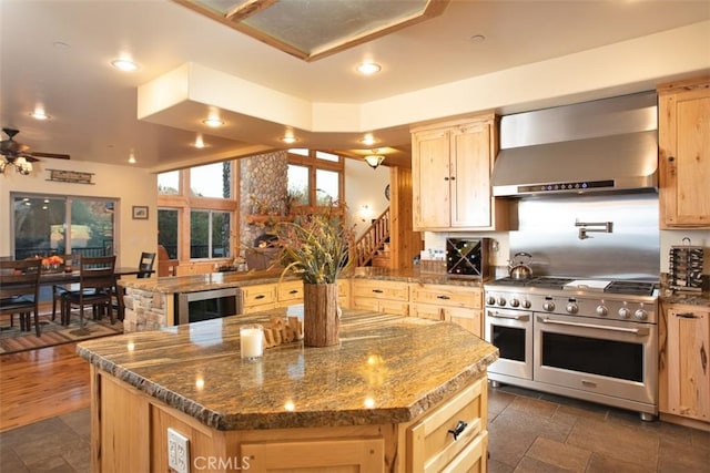 kitchen with wine cooler, range with two ovens, light brown cabinets, a kitchen island, and wall chimney range hood