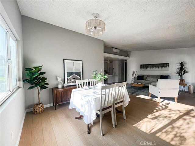 dining space with light wood-type flooring, an inviting chandelier, and a textured ceiling