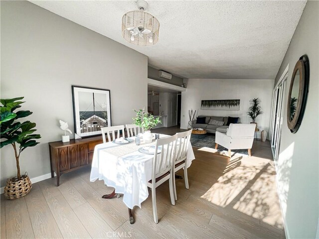 dining area with light hardwood / wood-style floors, a textured ceiling, and a notable chandelier