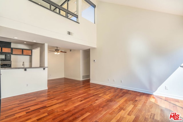 unfurnished living room featuring a high ceiling, ceiling fan, and light hardwood / wood-style flooring