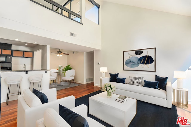 living room with ceiling fan, a high ceiling, and hardwood / wood-style floors