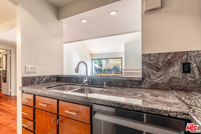 kitchen featuring hardwood / wood-style flooring, dark stone counters, vaulted ceiling, stainless steel dishwasher, and sink