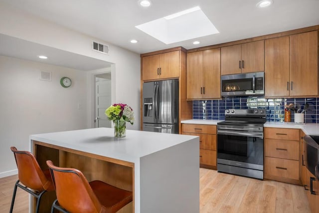 kitchen with tasteful backsplash, a center island, a skylight, light wood-type flooring, and appliances with stainless steel finishes