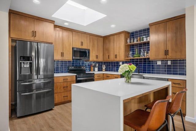 kitchen with appliances with stainless steel finishes, a skylight, tasteful backsplash, a kitchen island, and light wood-type flooring