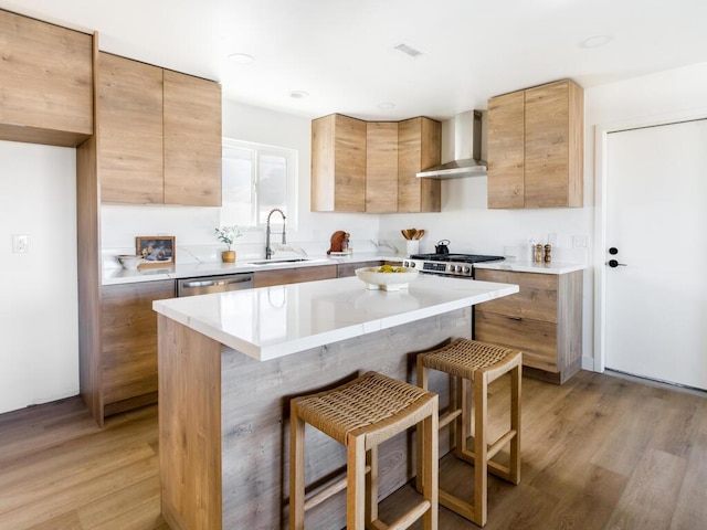 kitchen featuring wall chimney range hood, a kitchen island, sink, light wood-type flooring, and a kitchen breakfast bar