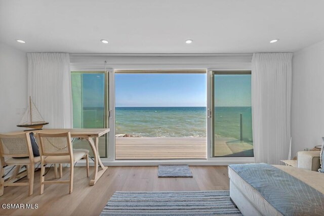 bedroom with a water view, light wood-type flooring, and a view of the beach