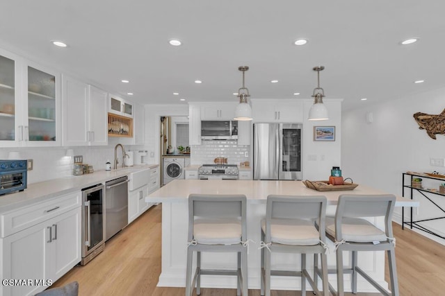 kitchen with white cabinetry, stainless steel appliances, a kitchen island, pendant lighting, and washer / clothes dryer