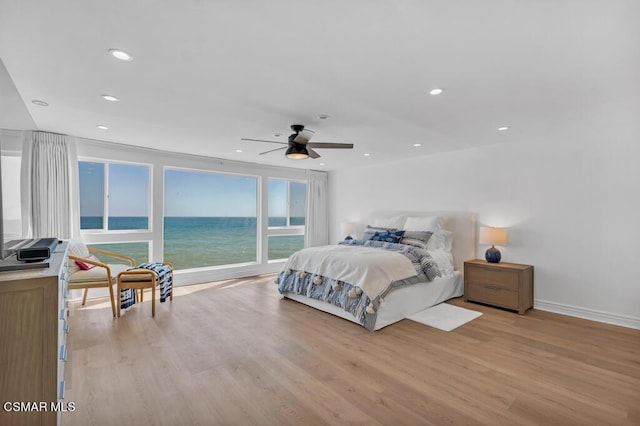 bedroom with ceiling fan, a water view, and light wood-type flooring