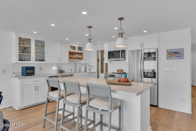 kitchen featuring pendant lighting, white cabinets, a kitchen island, stainless steel appliances, and light hardwood / wood-style flooring