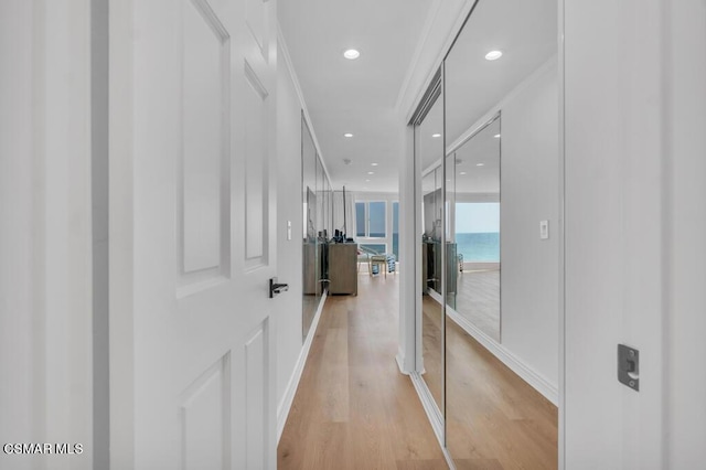 hall with ornamental molding, a water view, and light hardwood / wood-style flooring