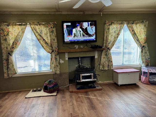 living room with ceiling fan, a wood stove, and hardwood / wood-style flooring