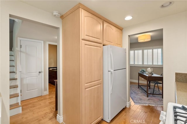 kitchen featuring light brown cabinets, white refrigerator, stove, and light hardwood / wood-style flooring