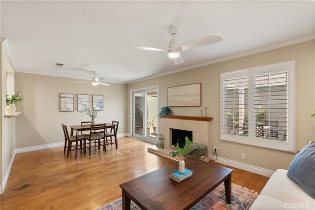 living room featuring ceiling fan, a tiled fireplace, ornamental molding, and hardwood / wood-style floors