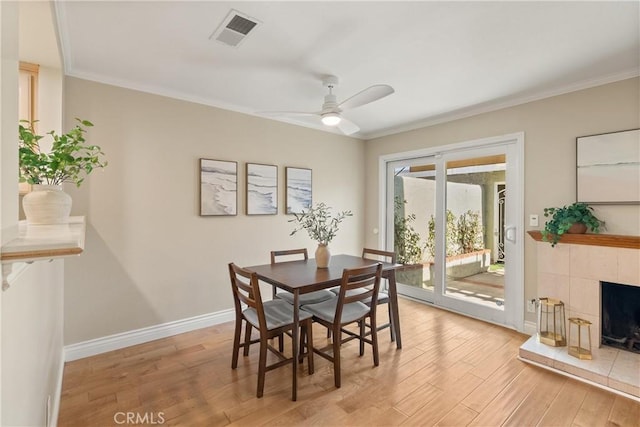 dining room with ceiling fan, a tile fireplace, crown molding, and light hardwood / wood-style floors