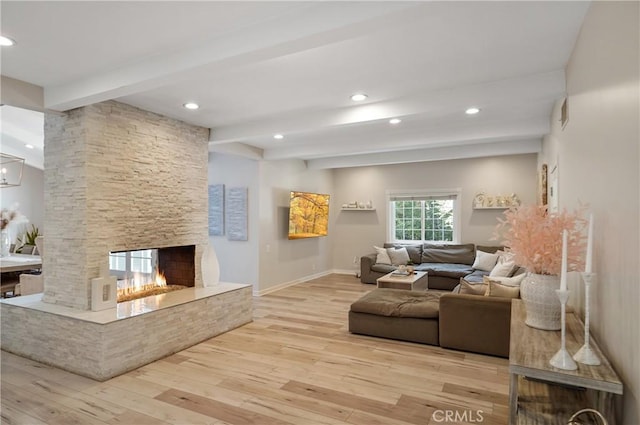 living room featuring beam ceiling, recessed lighting, light wood-style floors, a stone fireplace, and baseboards