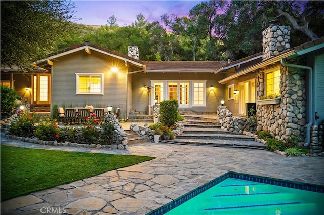 back of property featuring a chimney, an outdoor pool, and a patio