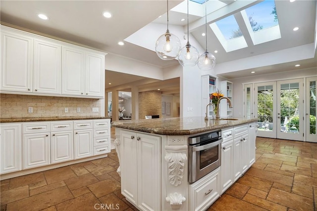 kitchen with an island with sink, white cabinetry, stainless steel oven, and stone tile flooring